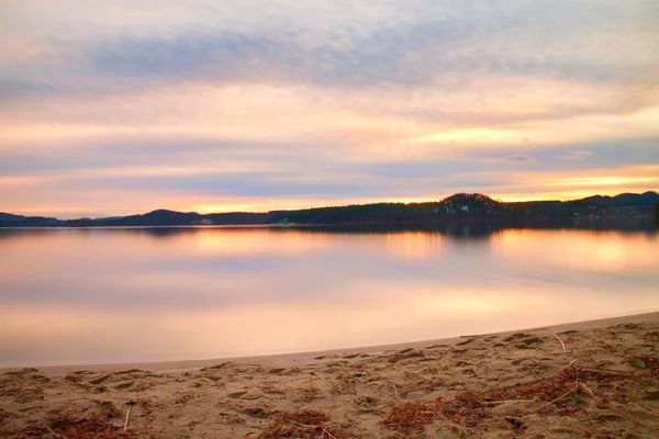 Praia abandonada no lago antes do pôr-do-sol do outono, raios de sol entre nuvens e reflexões no nível da água — Fotografia de Stock