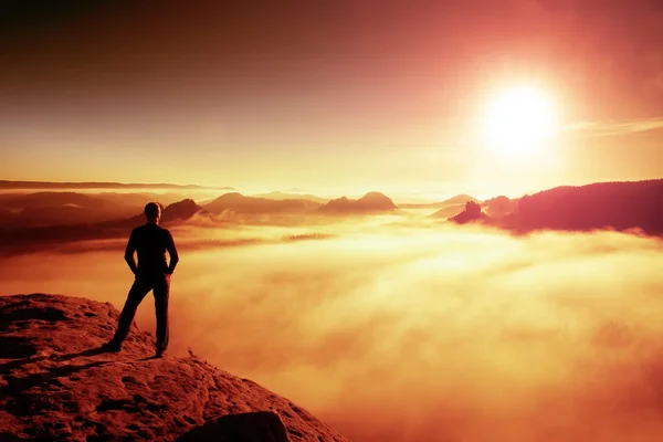 Hiker in black stands on rock abve valley within daybreak and watch to Sun. Beautiful moment the miracle of nature — Stock Photo, Image