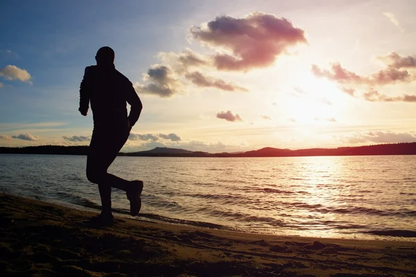 Silhouet van sport actieve man uitgevoerd en uitoefening op strand bij levendige kleurrijke zonsondergang. — Stockfoto