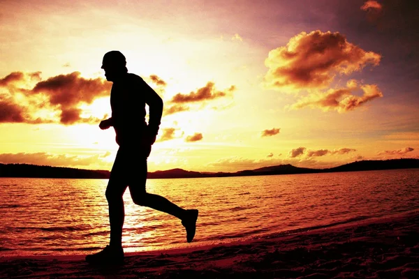 Silhouette of sport active man running and exercising on beach at vivid colorful sunset. — Stock Photo, Image