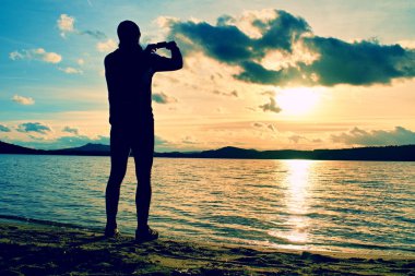 Uzun boylu adam günbatımı cep telefonu ile fotoğraf çekmek. Deniz kıyı şeridi, sonbahar günü