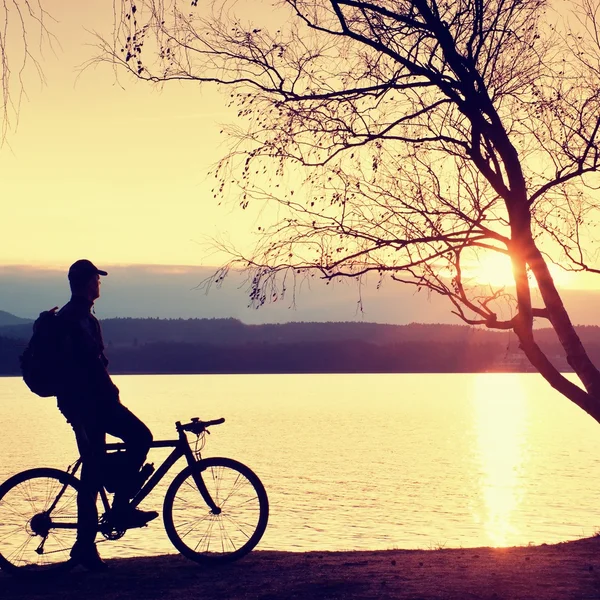 Jovem silhueta ciclista no céu azul e fundo do pôr do sol na praia. Fim de estação no lago . — Fotografia de Stock