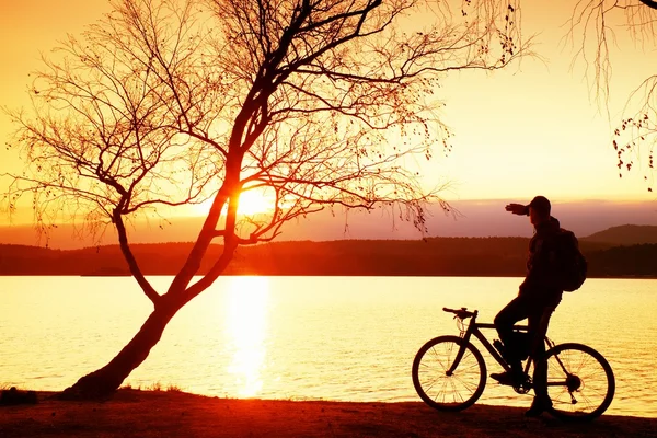 Joven silueta ciclista en el cielo azul y fondo de la puesta del sol en la playa. Fin de temporada en el lago . — Foto de Stock