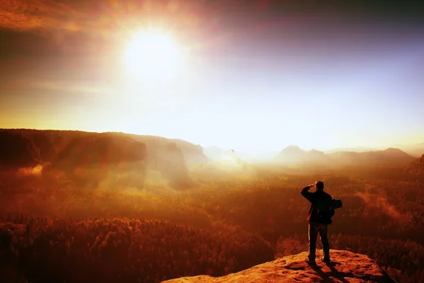 Red filter photo. Tourist with backpack and poles on  rocky peak. Dreamy fogy valley below — Stok fotoğraf