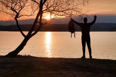 El havada olan adam. Uzun boylu ile sportif sırt çantası standları plajda koyu spor giyim uzun yürüyüşe çıkan kimse zevk günbatımı ufuktan