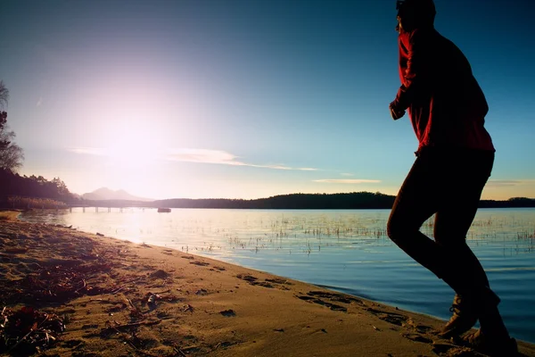Sylwetka sport aktywny dorosły człowiek działa i ćwiczenia na plaży. Spokojne wody, wyspa i tło niebo zachód słońca. — Zdjęcie stockowe