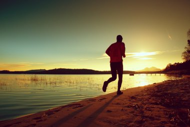 Uzun boylu adam pembe windcheater ve karanlık kap gün batımında sahilde koşmak
