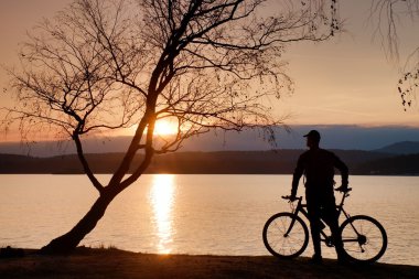 Genç adam bisikletçi siluet pembe turuncu gökyüzü ve sahilde günbatımı arka plan.