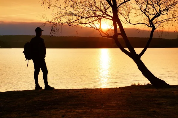 Homme avec la main en l'air. Grand randonneur en vêtements de sport sombres avec des stands de sac à dos sportif sur la plage profiter du coucher de soleil à l'horizon — Photo