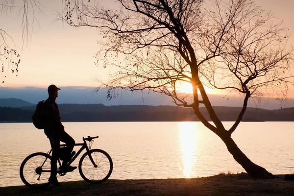 Giovane silhouette ciclista su cielo blu e sfondo tramonto sulla spiaggia. Fine stagione al lago . — Foto Stock