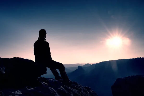 Turystyczny odpocząć. Przystojny młody mężczyzna siedzi na skale i widokiem na mgliste góry skaliste. — Zdjęcie stockowe