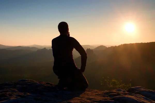 Sportsmann hiker in black sportswear sit on mountain top and take a rest. Tourist  watch down to morning misty valley. — Stock Photo, Image