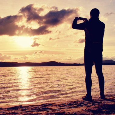 Cep telefonu ve sonbahar günbatımı veya gündoğumu alarak resmini pitoresk deniz sahne tutan sporcu. Sezon sonunda resort.
