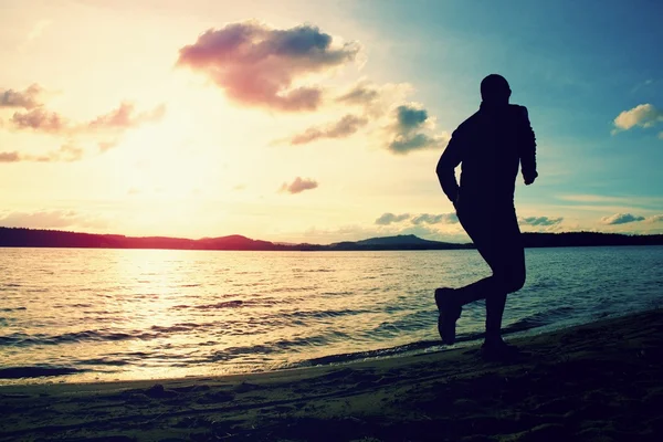 Deportista alto correr a lo largo de la costa del mar de salida del sol detrás, playa vacía — Foto de Stock