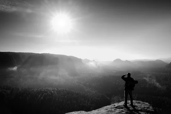 Tourist mit Rucksack und Stöcken auf felsigem Gipfel. sonniger Tag, verträumtes Nebeltal unten — Stockfoto