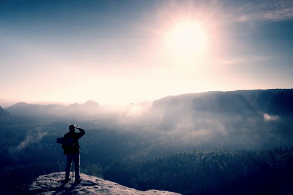 Tourist mit Rucksack und Stöcken auf felsigem Gipfel. sonniger Tag, verträumtes Nebeltal unten — Stockfoto