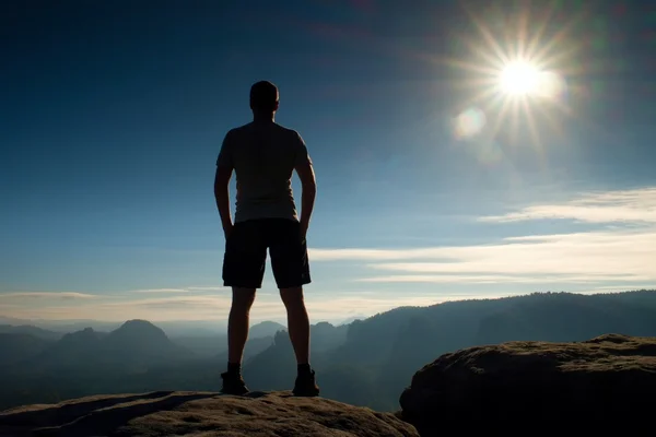 Caminante solo en pantalones negros se paran en el imperio del rock y vigilan el brumoso y brumoso valle de la mañana hasta el sol . — Foto de Stock