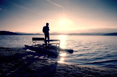 Sırt çantası ile uzun boylu turizm günbatımında pedallı bot, sahilde yürümek. Sonbahar denizde
