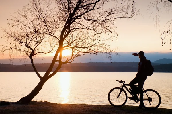 Jovem silhueta ciclista no céu azul e fundo do pôr do sol na praia. Fim de estação no lago . — Fotografia de Stock