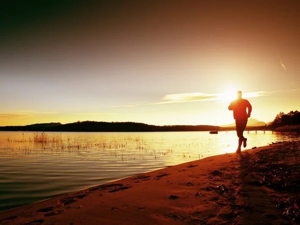 Sportieve Man doen ochtend joggen op zee strand van Bright Sunrise silhouetten — Stockfoto