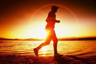 Kumsalda Runner güneş ışınları. Beyzbol şapkalı sporcu deniz üzerinde gündoğumu sırasında koşu