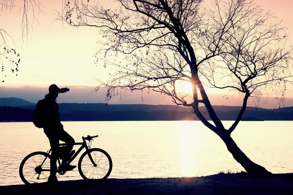 Young cyclist silhouette on blue sky and sunset background on beach. End of season at lake. — Stock Photo, Image