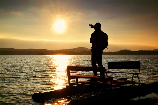 Sylwetka turysta z plecaka na opuszczonych wodnym w zachód słońca. Jesienne słońce nad morze — Zdjęcie stockowe