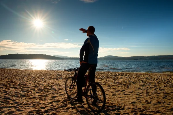 Jovem ciclista silhueta no céu azul e pôr do sol de fundo na praia. Fim de estação no lago . — Fotografia de Stock