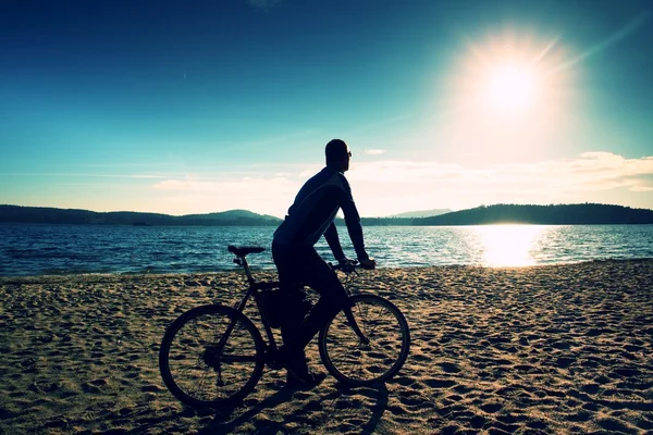 Jovem ciclista silhueta no céu azul e pôr do sol de fundo na praia. Fim de estação no lago . — Fotografia de Stock