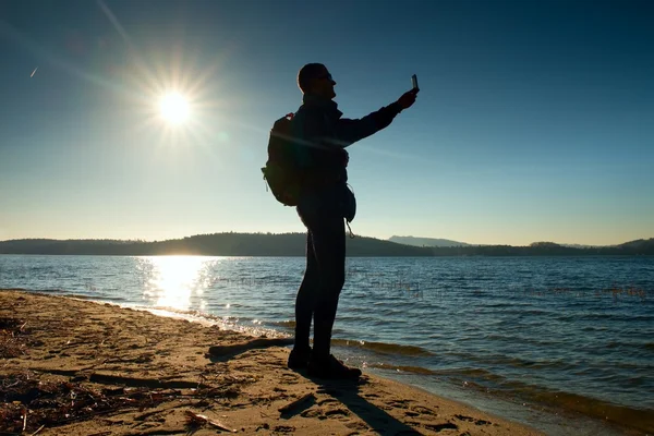 Człowiek posiadający telefon, biorąc obraz jesienią zachód lub wschód słońca w morze malowniczej scenerii — Zdjęcie stockowe