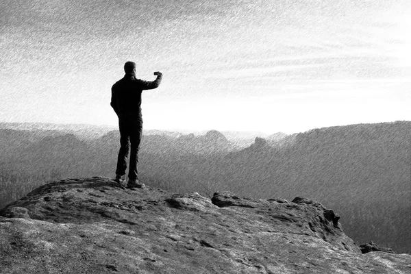 Schwarz-weiß gestrichelte Retro-Skizze. Wanderer fotografiert mit dem Smartphone auf dem Gipfel des Felsens — Stockfoto