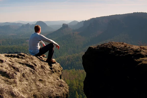 Молодий чоловік у чорному спортивному одязі сидить на краю скелі і дивиться, щоб помилитися в долині — стокове фото