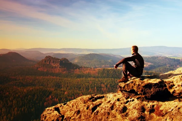 Отдыхающий человек на вершине скалы с воздушным видом на глубокую туманную долину — стоковое фото