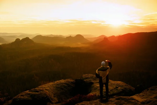 Mann fotografiert mit Smartphone auf Gipfel des Rock-Imperiums verträumte nebelige Landschaft, frühlingshafte Orange in einem wunderschönen Tal des Sächsischen Schweiz Parks. — Stockfoto