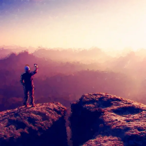 Tinta aquarela. Efeito de pintura. Homem tira fotos com telefone inteligente no pico do império rock. Paisagem nebulosa sonhadora, primavera laranja rosa nebuloso nascer do sol nas montanhas . — Fotografia de Stock