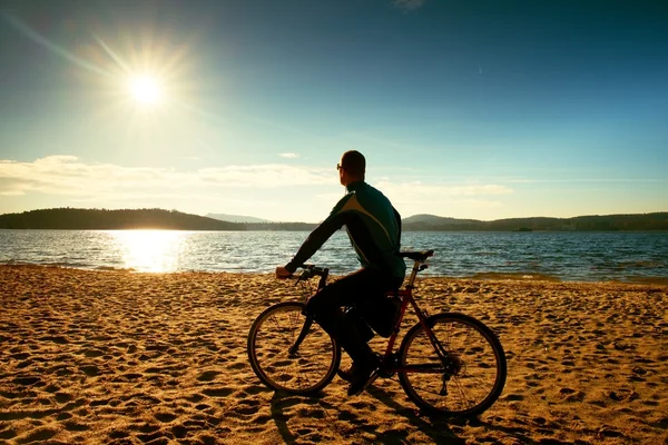 Jovem ciclista silhueta no céu azul e pôr do sol de fundo na praia. Fim de estação no lago . — Fotografia de Stock