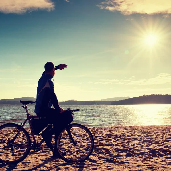 Jovem ciclista sentar em bicicleta, céu azul e pôr do sol de fundo na praia. Fim de temporada no lago e popular resort turístico.. Vivid e forte efeito vinheta . — Fotografia de Stock