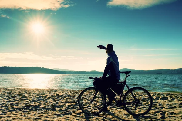 Jovem ciclista sentar em bicicleta, céu azul e pôr do sol de fundo na praia. Fim de temporada no lago e popular resort turístico.. Vivid e forte efeito vinheta . — Fotografia de Stock