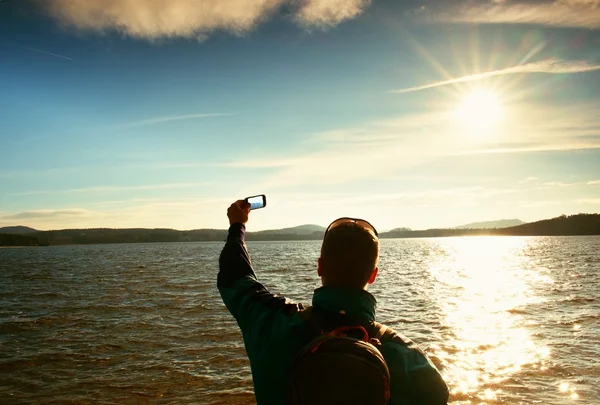 Tall ginger hair man tourist taking photos or video with mobile phone. Autumn sunny day at sea