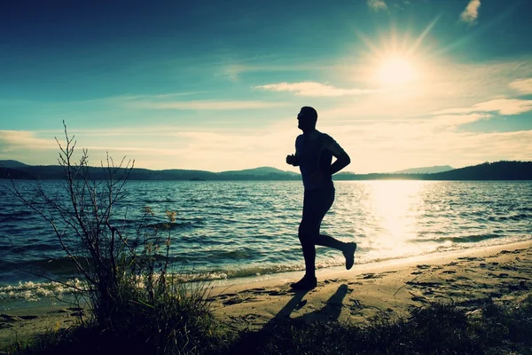 Silueta sportovní aktivní člověk běží a cvičení na pláži v busch pod západ slunce. — Stock fotografie