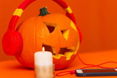 Mutlu oyulmuş balkabağı Cadılar Bayramı dekorasyon festivali ve müzik konsepti arka planda. Çeşitli mum parçalarıyla turuncu arka planda kabak dinleten radyoyu karıştır..