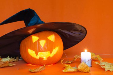 Turuncu bir masanın üzerinde yanan mumların yanında siyah bir cadı şapkası olan bir fener. Stüdyo turuncu moda duvar.