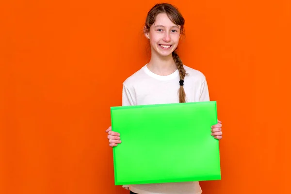 白いTシャツの若いブルネットの若い女子高生は 文書で明るい緑のフォルダを保持しています オレンジ色のスタジオ撮影 — ストック写真