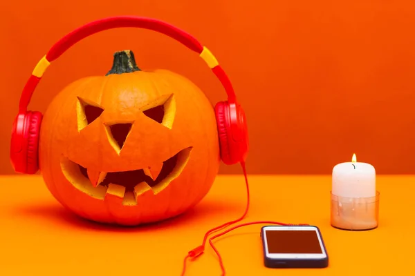 Happy carved pumpkin Halloween decorations festival and music concept background.Mix variety candle items and pumpkin listening radio by headphone on orange background.