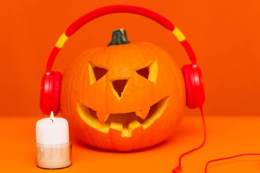 Cadılar Bayramı dekorasyon festivaliniz ve müzik konseptiniz kutlu olsun. Çeşitli mum parçalarıyla turuncu arka planda radyo dinleyen balkabağını karıştır..