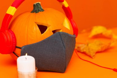 Fron view Mutlu Cadılar Bayramı dekorasyonları festivali ve müzik konsepti arka planda. Çeşitli mum parçalarını karıştır maske ve turuncu arka planda kulaklıkla radyo dinleyen balkabağı.