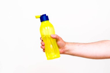 Görüntüyü kapat. Adamın eli, beyaz arka planda izole edilmiş sarı su şişesini tutuyor..