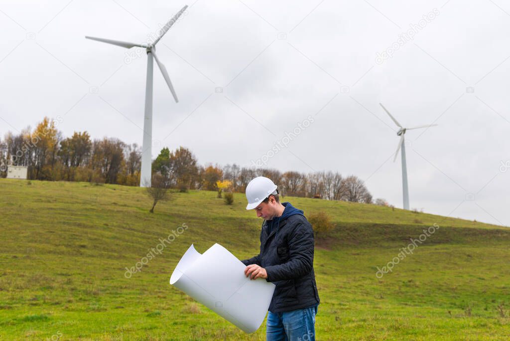 male engineer holding a plan at wind turbine at autumn cloudy sky green meadow outdoors