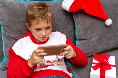 Noel 'de akıllı telefon kullanan çekici bir çocuk. Evdeki Xmas fotoğrafı için beyaz hediye.