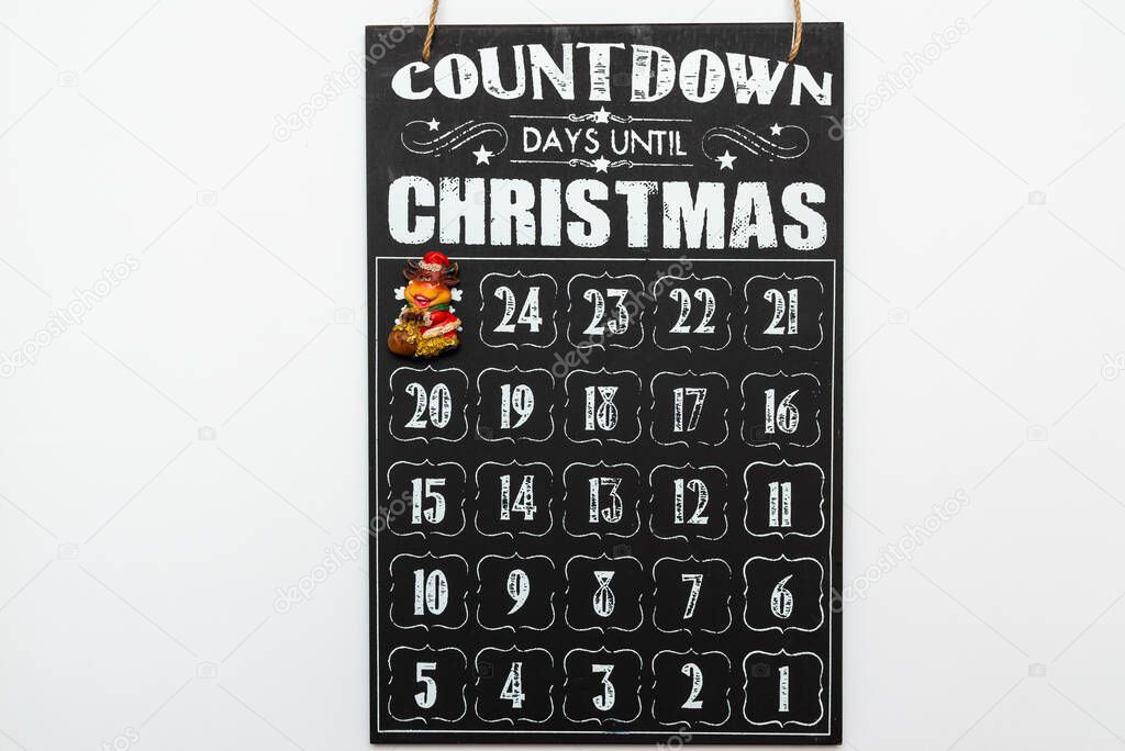 Toy bull on black wooden advent calendar showing Christmas countdown top view flat lay white background.
